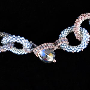 May include: A beaded necklace with a chain link design in shades of blue and pink with a crystal pendant.