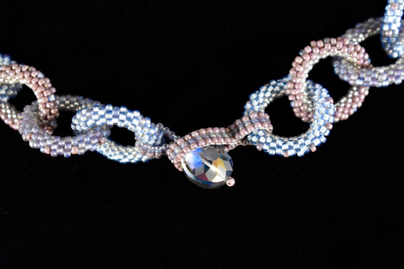 May include: A beaded necklace with a chain link design in shades of blue and pink with a crystal pendant.