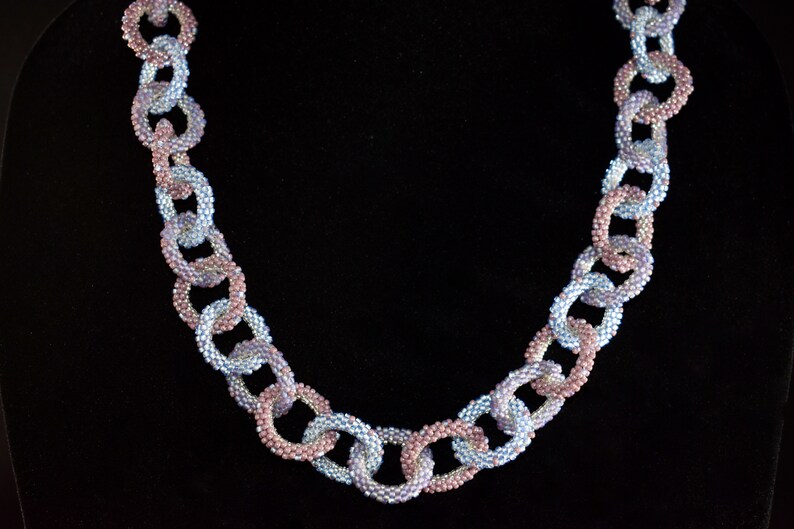 May include: A necklace made of linked, beaded loops. The loops are alternating colors of light blue and pink.