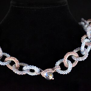 May include: A silver and rose gold beaded necklace with a large crystal pendant. The necklace is made of small, round beads that are strung together in a chain-like pattern.