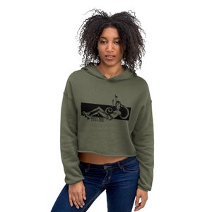 Peut inclure: Un sweat &agrave; capuche court de couleur olive avec un motif noir repr&eacute;sentant une femme sur des patins &agrave; roulettes. Le motif comprend le texte "PUNK EGO".