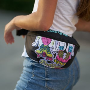 May include: A black fanny pack with a colorful graphic print of roller skaters. The print features girls wearing colorful roller skates and the text "Rad Gal" on the front.