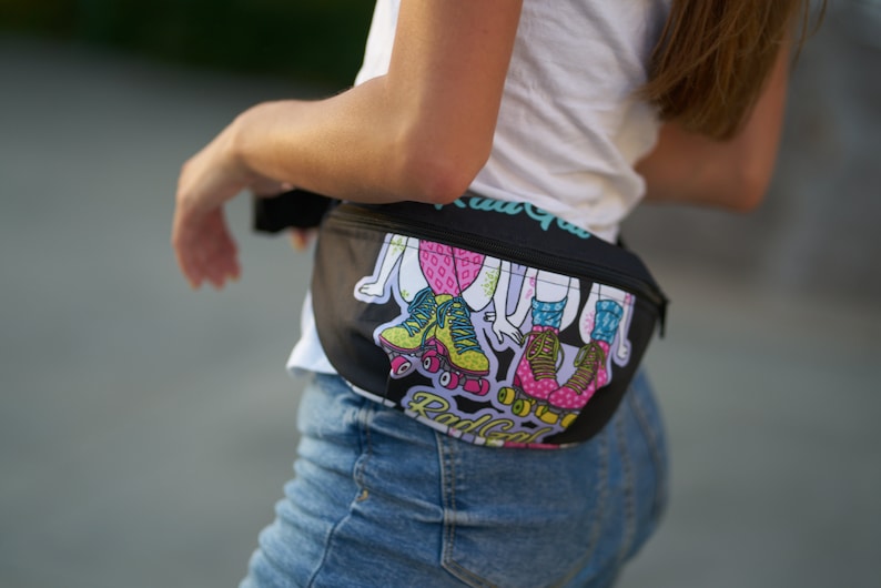 May include: A black fanny pack with a colorful graphic print of roller skaters. The print features girls wearing colorful roller skates and the text "Rad Gal" on the front.