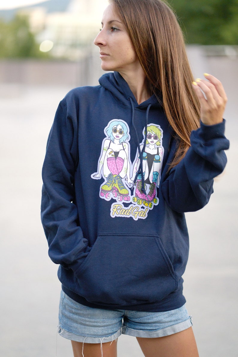 Puede incluir: Una sudadera con capucha azul marino con un gr&aacute;fico de dos mujeres en patines. El gr&aacute;fico incluye el texto "Rad Gal".
