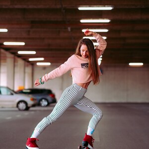 Peut inclure: Une femme portant une chemise rose &agrave; rayures et un pantalon noir et blanc &agrave; rayures fait du roller dans un parking. Elle porte des rollers rouges avec des roues blanches.