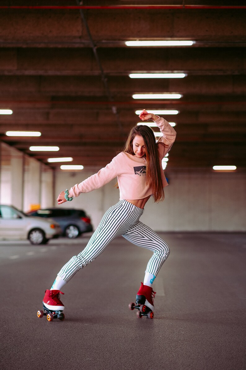 Peut inclure: Une femme portant une chemise rose &agrave; rayures et un pantalon noir et blanc &agrave; rayures fait du roller dans un parking. Elle porte des rollers rouges avec des roues blanches.
