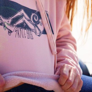 Peut inclure: Un sweat &agrave; capuche rose avec un graphique d'une personne faisant du skateboard et le texte "Skate Eagle".