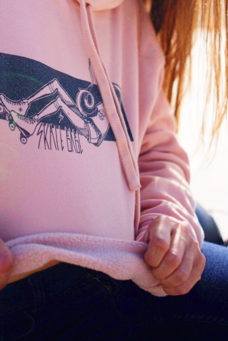 Peut inclure: Un sweat &agrave; capuche rose avec un graphique d'une personne faisant du skateboard et le texte "Skate Eagle".