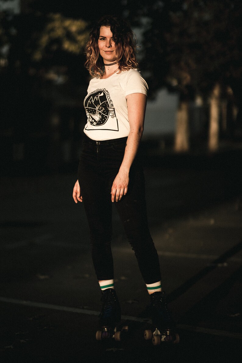 May include: A woman wearing a white t-shirt with a black graphic print and black pants is roller skating. She is wearing green and white striped socks and black roller skates.