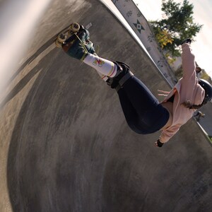 Op de afbeelding: Een persoon met rollerskates en een roze hoodie skatet in een betonnen halfpipe.