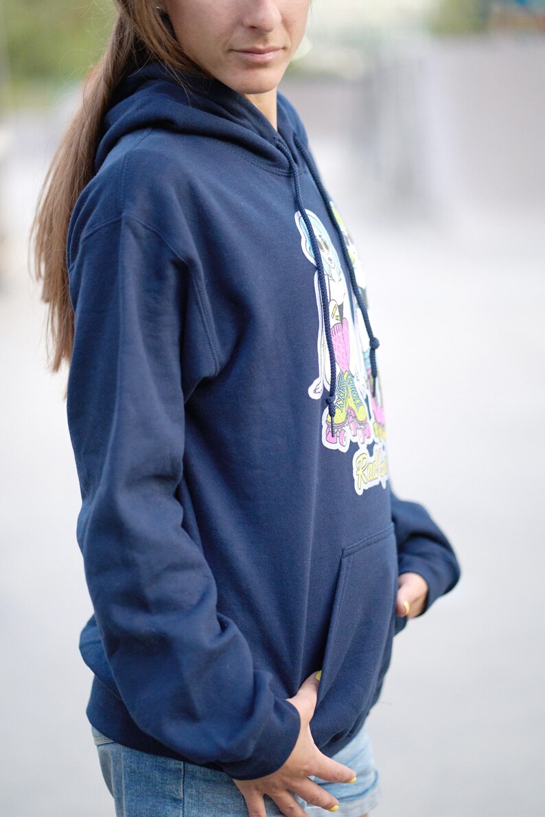 Puede incluir: Una sudadera con capucha azul marino con un gr&aacute;fico de dos personas patinando. El gr&aacute;fico es en rosa, azul, amarillo y verde. La sudadera tiene un bolsillo canguro.