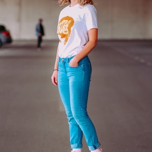 May include: A woman wearing a white t-shirt with a gold graphic and blue jeans is roller skating. She is wearing pink roller skates with white wheels.
