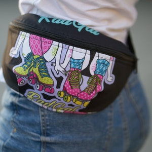 May include: Black fanny pack with a colorful graphic of roller skaters. The text "Rad Gal" is printed on the pack.