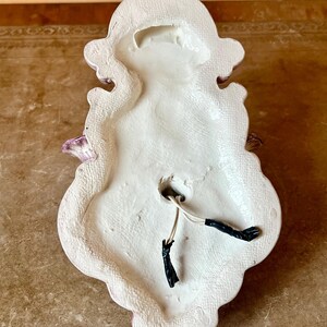 May include: The back of a white ceramic wall sconce with a pink floral design. The sconce has two electrical wires coming out of the back.
