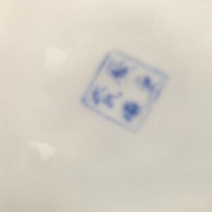 May include: Close-up of a blue and white stamp on a white surface. The stamp is square and has a design of a flower with a circle in the center.