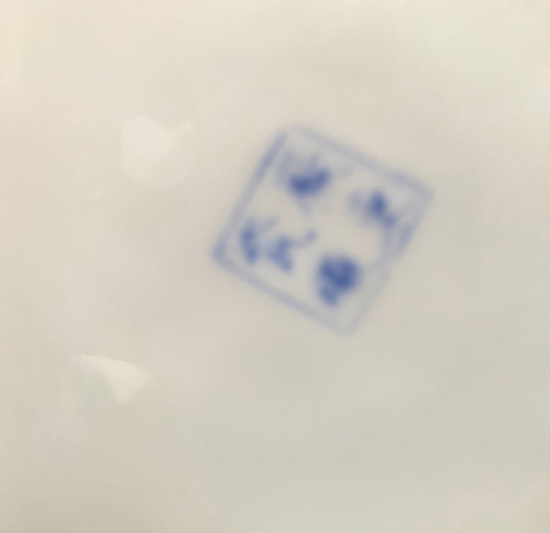 May include: Close-up of a blue and white stamp on a white surface. The stamp is square and has a design of a flower with a circle in the center.