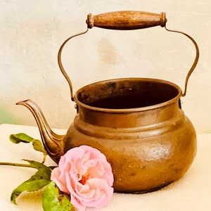 Può includere: Una teiera di rame vintage con un manico in legno e una rosa rosa.
