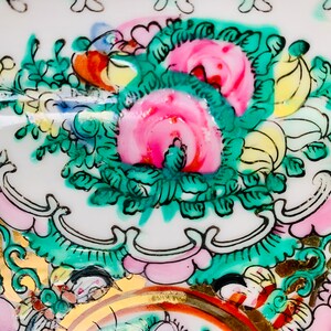 May include: Close-up of a white porcelain plate with a floral design. The design features pink, green, and yellow flowers with gold accents.