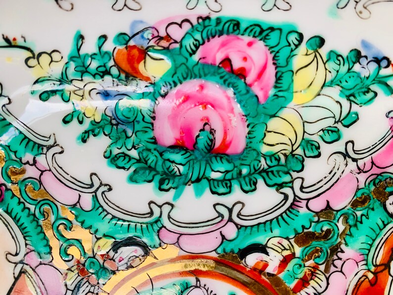 May include: Close-up of a white porcelain plate with a floral design. The design features pink, green, and yellow flowers with gold accents.