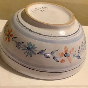 Può includere: Una ciotola in ceramica bianca con un motivo floreale blu e arancione. La ciotola è dipinta a mano e ha le parole "Dipinto a mano" scritte sul fondo.