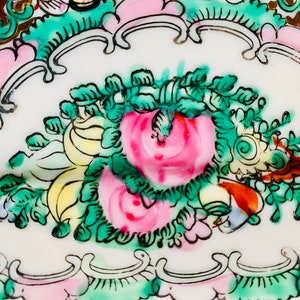 May include: Close-up of a white porcelain plate with a floral design. The design features pink, green, and yellow flowers with gold accents.