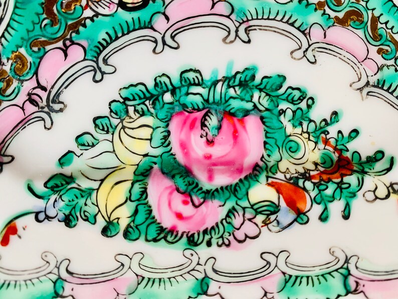 May include: Close-up of a white porcelain plate with a floral design. The design features pink, green, and yellow flowers with gold accents.