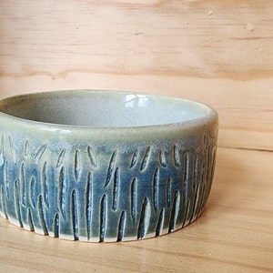 Puede incluir: Un pequeño cuenco redondo de cerámica con un esmalte verde claro y un esmalte azul oscuro con un patrón texturizado de líneas verticales.