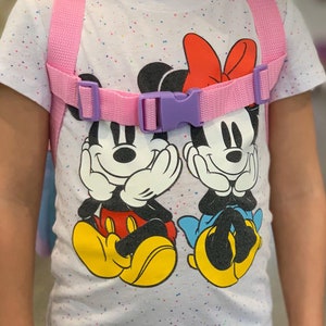 Puede incluir: Una mochila infantil rosa y morada con correas ajustables. La mochila presenta una camiseta blanca con un estampado de lunares de colores y un gr&aacute;fico de Mickey Mouse y Minnie Mouse.