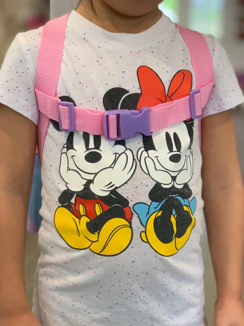 Puede incluir: Una mochila infantil rosa y morada con correas ajustables. La mochila presenta una camiseta blanca con un estampado de lunares de colores y un gr&aacute;fico de Mickey Mouse y Minnie Mouse.