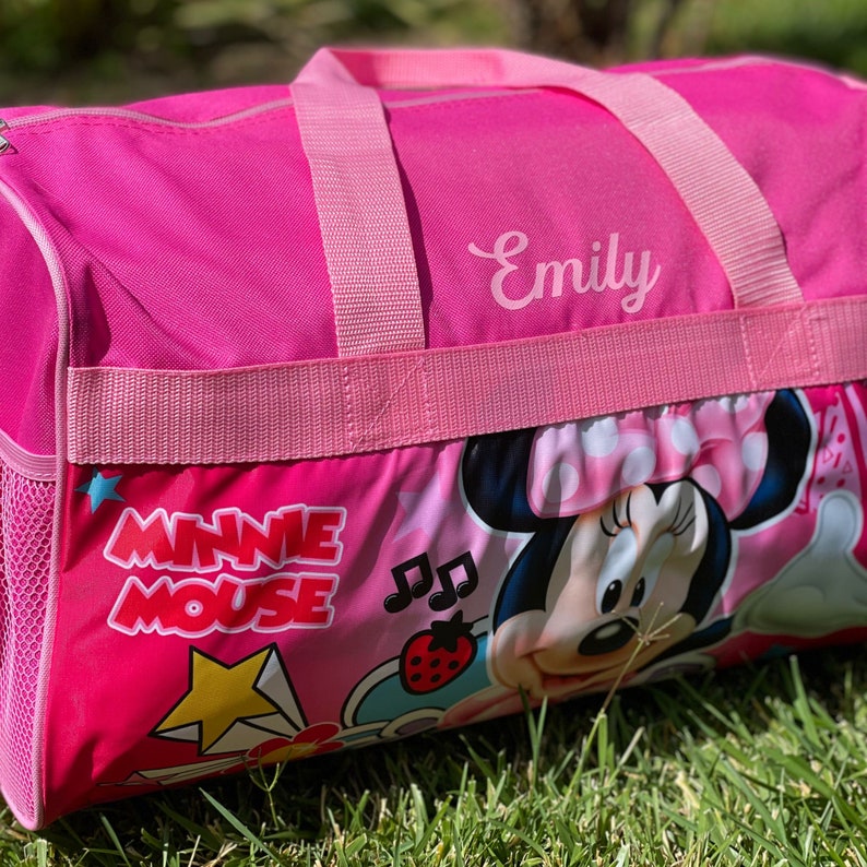 May include: Pink Minnie Mouse themed duffel bag with a white mesh pocket and a pink strap. The bag has the name "Emily" embroidered on the front.