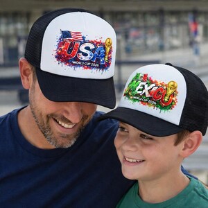 Puede incluir: Gorras de camionero en blanco y negro con panel frontal blanco. Una gorra muestra "USA" con la bandera estadounidense y un trofeo dorado, la otra "MEXICO" con un trofeo dorado. Ambas gorras tienen el texto "WORLD CUP 2026".