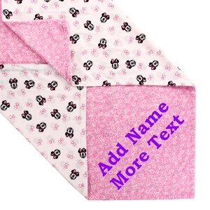 K&ouml;nnte beinhalten: Eine rosa und wei&szlig;e Decke mit einem Minnie Mouse-Druck. Die Decke ist in der H&auml;lfte gefaltet und die untere H&auml;lfte tr&auml;gt den Text "Add Name More Text" in Lila.