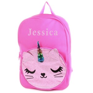 May include: Pink backpack with a unicorn cat face on the front. The backpack has the name "Jessica" embroidered on the front.