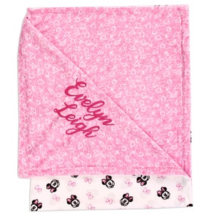 K&ouml;nnte beinhalten: Rosa-wei&szlig;e Babydecke mit einem Minnie Mouse-Design auf der einen Seite und einem rosa Hintergrund mit wei&szlig;en Herzen und dem gestickten Namen "Evelyn Leigh" auf der anderen Seite.