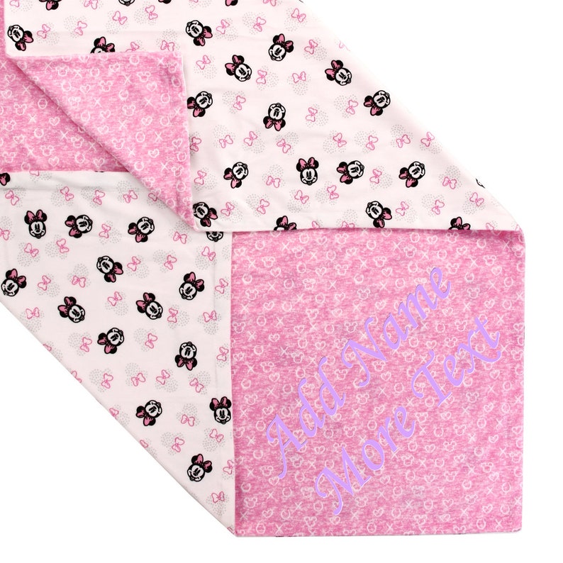 K&ouml;nnte beinhalten: Eine rosa und wei&szlig;e Babydecke mit einem Minnie Mouse-Druck auf der einen Seite und einer rosa Seite mit dem Text "Add Name More Text" in Lila.
