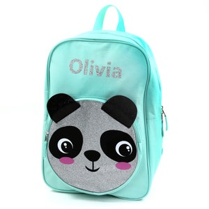 May include: A turquoise blue backpack with a silver glitter panda face on the front. The backpack has a zipper closure and a name tag that says "Olivia".