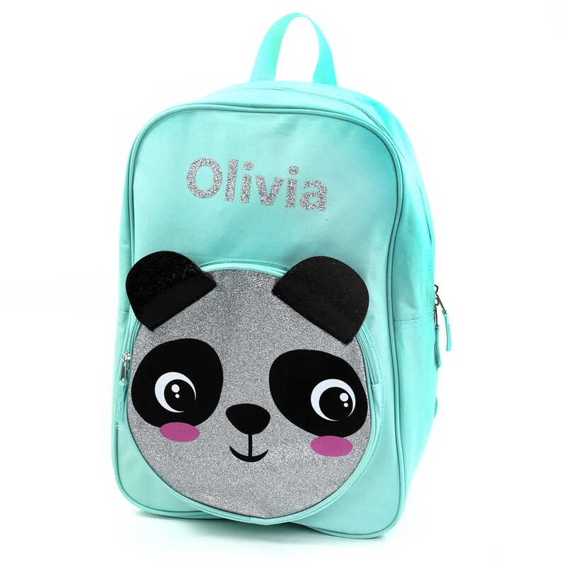 May include: A turquoise blue backpack with a silver glitter panda face on the front. The backpack has a zipper closure and a name tag that says "Olivia".