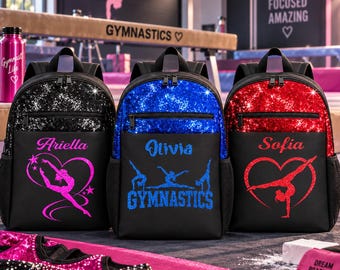 Op de afbeelding: Drie rugzakken met pailletten bovenkanten in zwart, blauw en rood. Elk heeft een naam en gymnastiek-afbeelding: Ariella met een roze hart-turnster, Olivia met blauwe tekst en Sofia met een rode hart-turnster. Inclusief zijvakken van gaas.