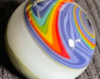 May include: A glass marble with a vibrant, swirling design in rainbow colours. The pattern includes red, orange, yellow, green, and blue, set against a white base. The marble has a glossy finish. A collectible item.