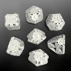 May include: Set of seven white dice with intricate designs and numbers 1 through 7. The dice are made of a hard plastic material and have a matte finish.