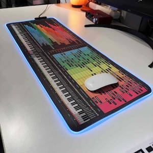 以下が含まれることがあります： キーボードをテーマにしたカラフルなマウスパッドで、白いマウスが載っています。マウスパッドは虹色のグラデーションで、黒い背景に白い文字と数字があります。