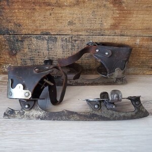 May include: A pair of vintage ice skates, featuring leather straps and metal blades. The skates show signs of wear and age, with a rustic aesthetic. The blades are attached to the leather boots with rivets, showcasing a classic design.