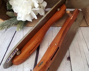 May include: Two vintage ice skate blades with wooden bases. The blades are silver and have a worn look. The wooden bases are brown and have a worn look. The blades are labelled "SKE-IIXX".