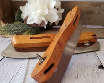 May include: Two vintage utility knives with wooden handles and metal blades. The blades are secured to the handles with screws. The handles are made of light brown wood and have a worn appearance.