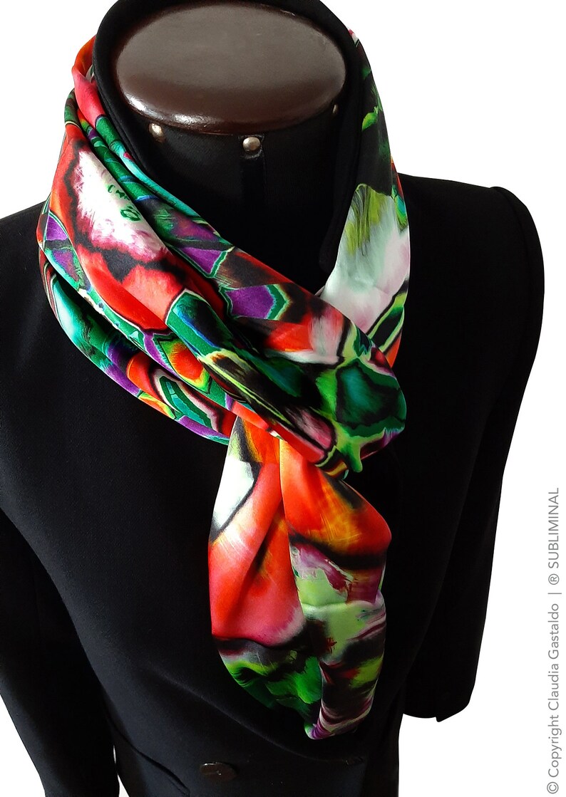 May include: A colorful silk scarf with abstract floral patterns in shades of red, green, purple, and white. The scarf is tied around a black mannequin's neck.