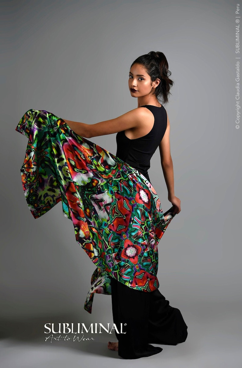 May include: A woman wearing a black tank top and black pants with a colorful patterned scarf draped over her shoulders. The scarf has a vibrant mix of red, green, blue, and yellow colors. The text "SUBLIMINAL Art to Wear" is visible at the bottom of the image.