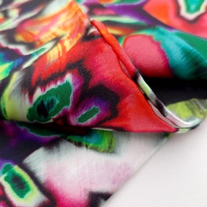 May include: Close-up of a colorful fabric with a swirling, abstract pattern in shades of red, green, purple, and yellow. The fabric is folded over, revealing a black background.