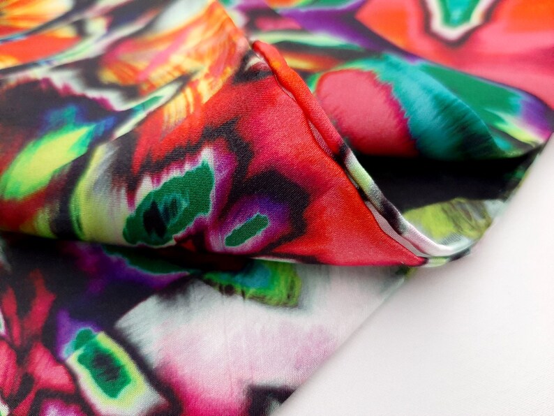 May include: Close-up of a colorful fabric with a swirling, abstract pattern in shades of red, green, purple, and yellow. The fabric is folded over, revealing a black background.