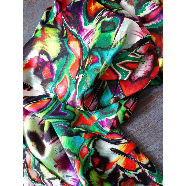 May include: A colorful abstract print fabric with shades of green, red, pink, yellow, and black. The fabric has a silky texture and is perfect for creating unique garments or accessories.