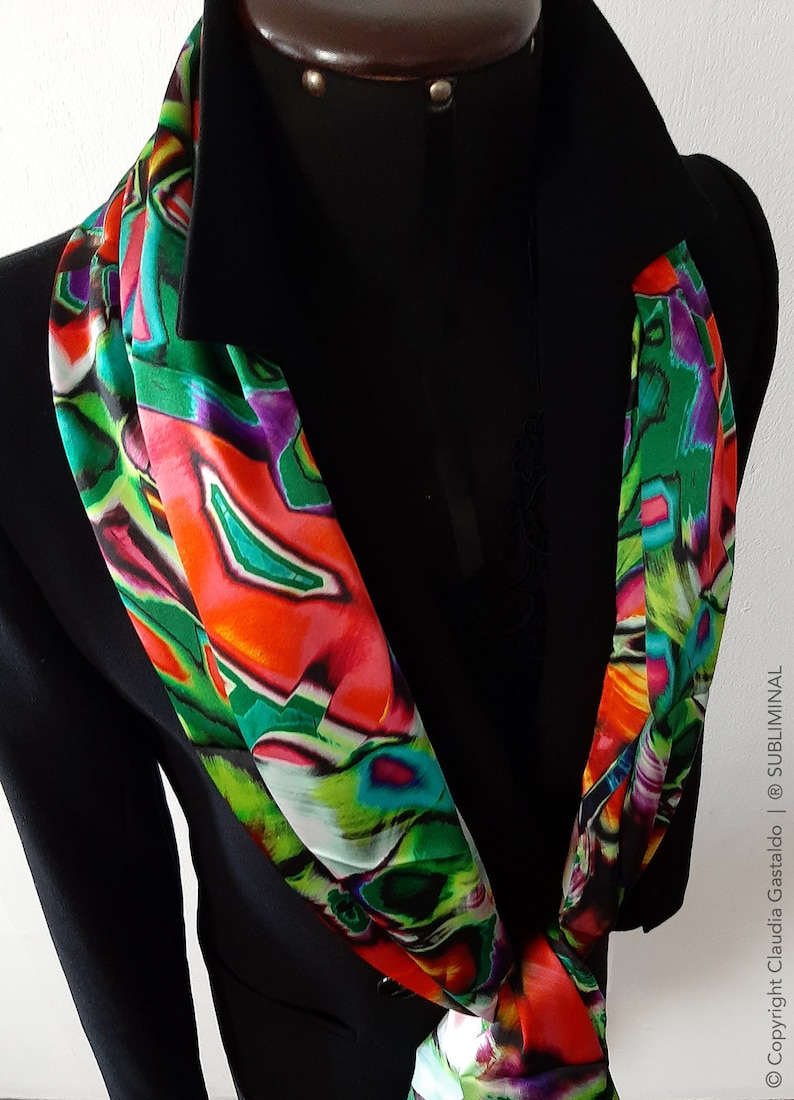 May include: A colorful abstract patterned scarf in shades of red, green, purple, and white. The scarf is tied around the neck of a black blazer.